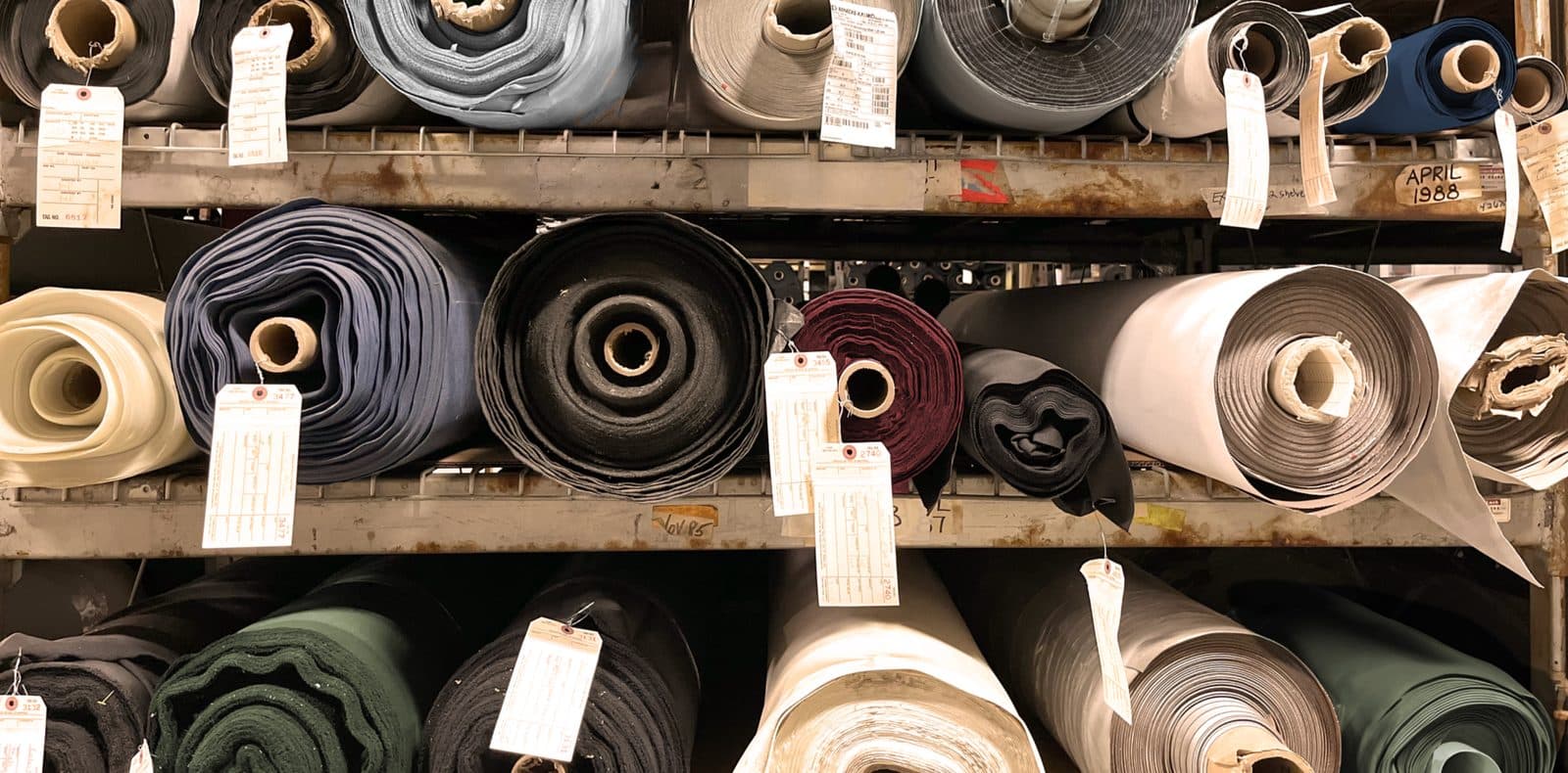 Paper-tagged textile rolls on warehouse racking at Core Products Group — handwritten inventory tag visible, automotive and contract-grade material